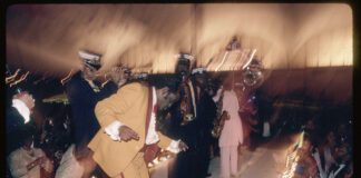 “Zulu Social Aid and Pleasure Club ball,” by Mitchel Osborne, depicts members of the Dejan’s Olympia Brass Band playing at a 1988 Mardi Gras ball. (THNOC; gift of Mitchel Osborne; 2007.0001.308 ©Mitchel Osborne)