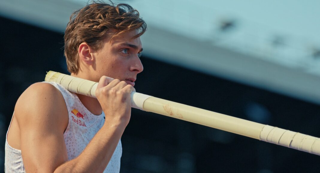 Pole vaulter Mondo Duplantis holds a pole on his shoulder and prepares for competition