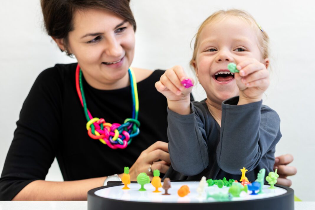 Toddler girl in child occupational therapy session doing sensory playful exercises with her therapist.