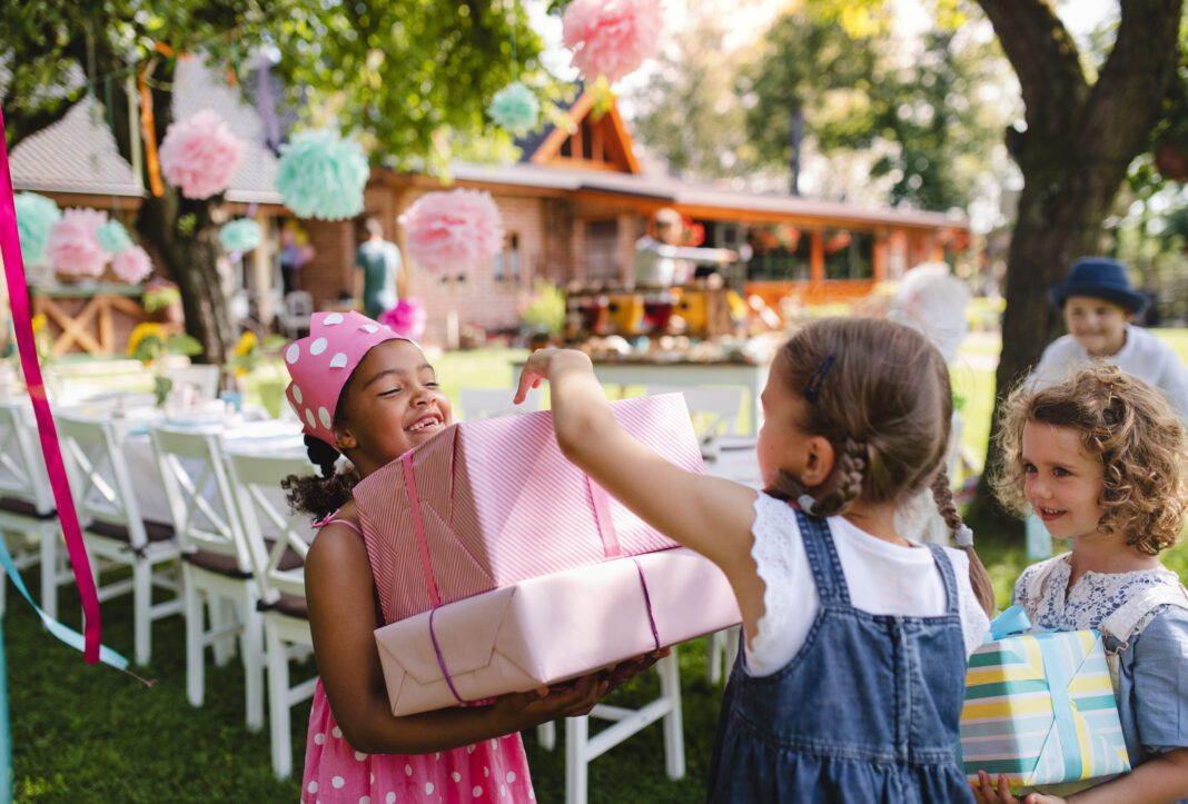 Portrait of small girl with friends and presents outdoors in garden in summer.